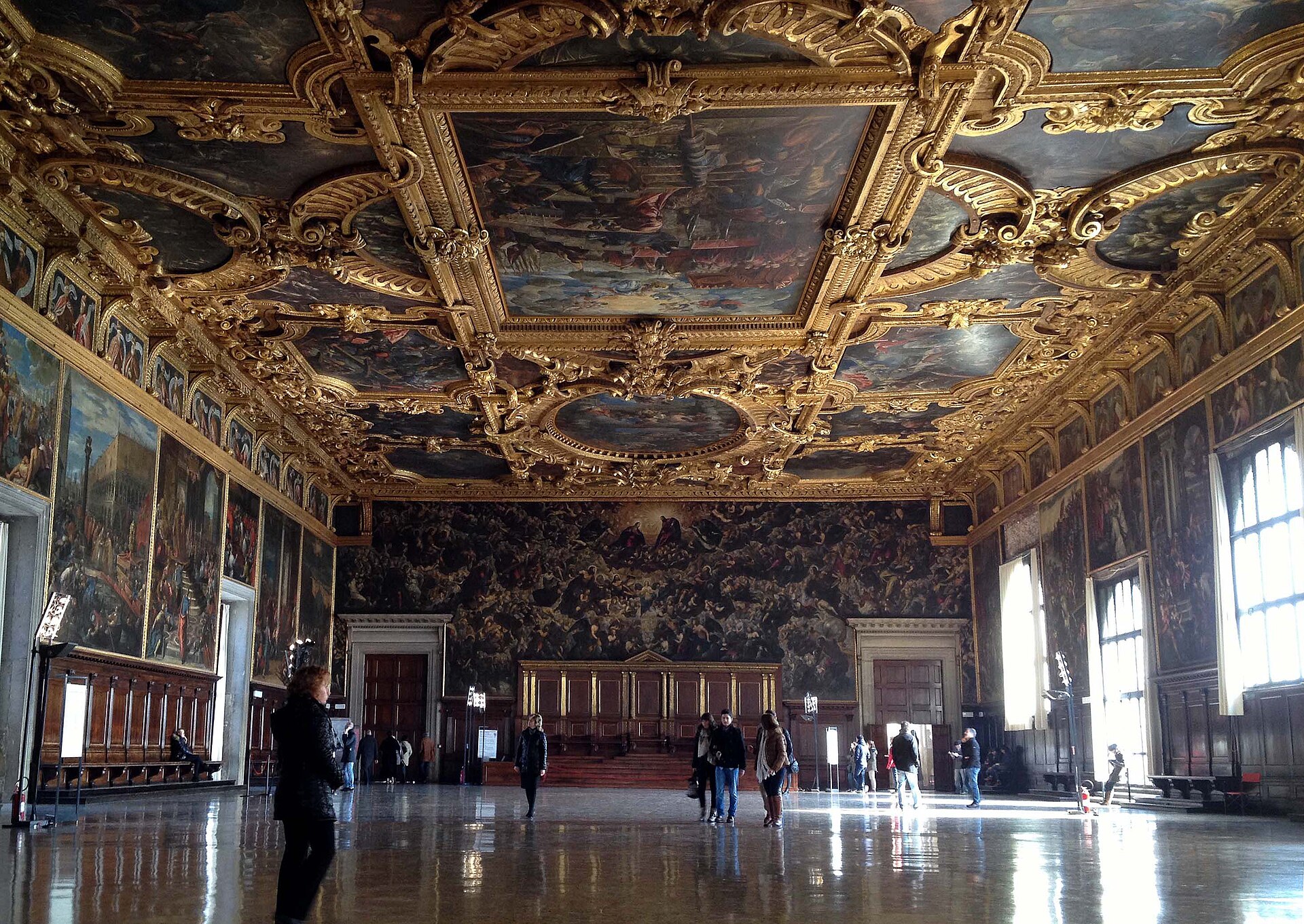 Interior of the Great Council Chamber with gilded ceiling, large historical canvases, windows and polished floor.