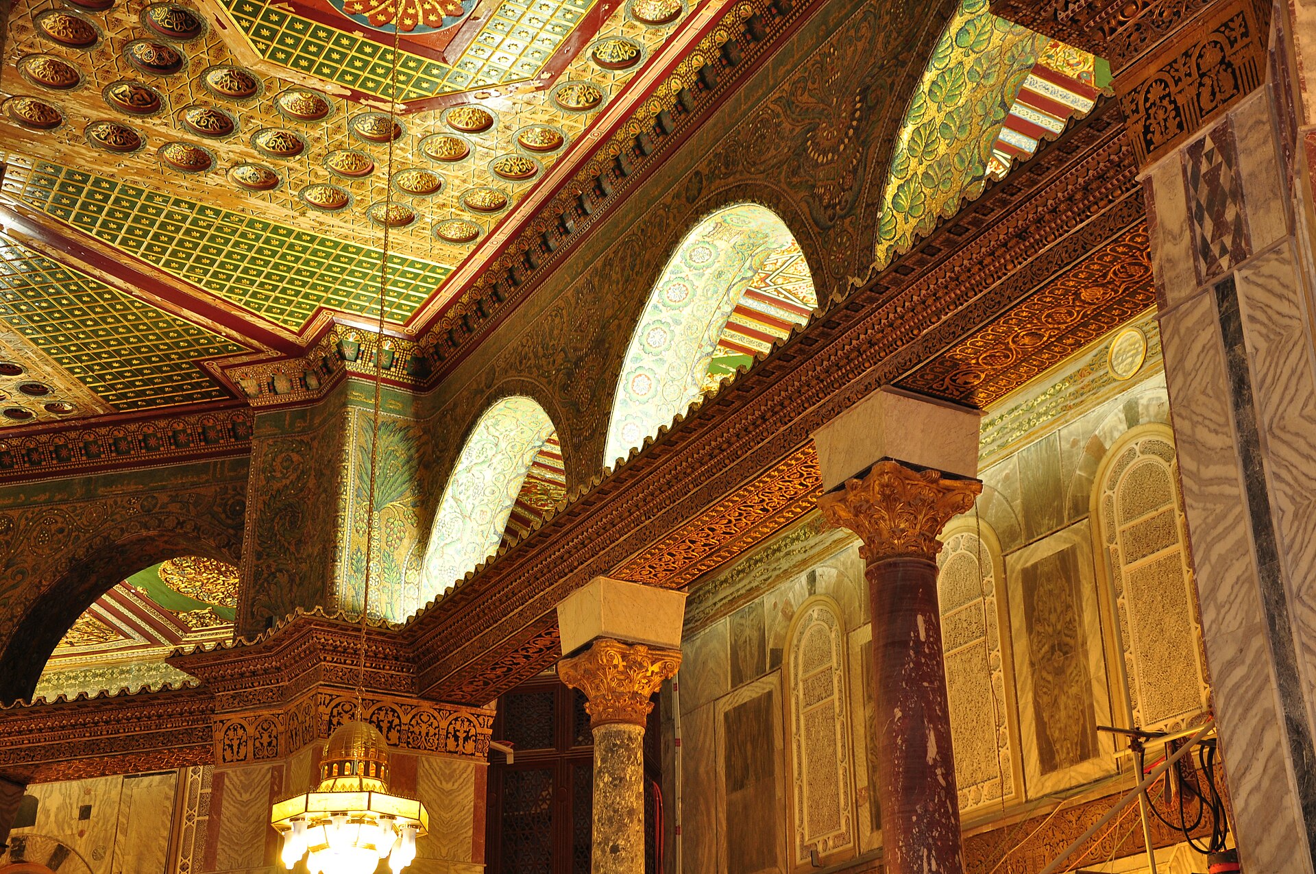 Interior piers, column capitals, decorated arches and screened windows beneath patterned ceiling fields.