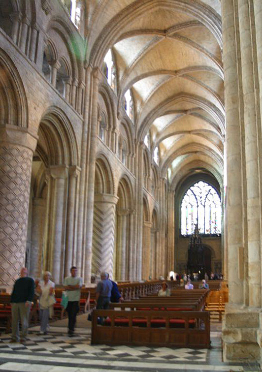 Oblique view along Durham Cathedral's nave arcade showing incised spiral and geometric drum piers, compound supports and vaults.