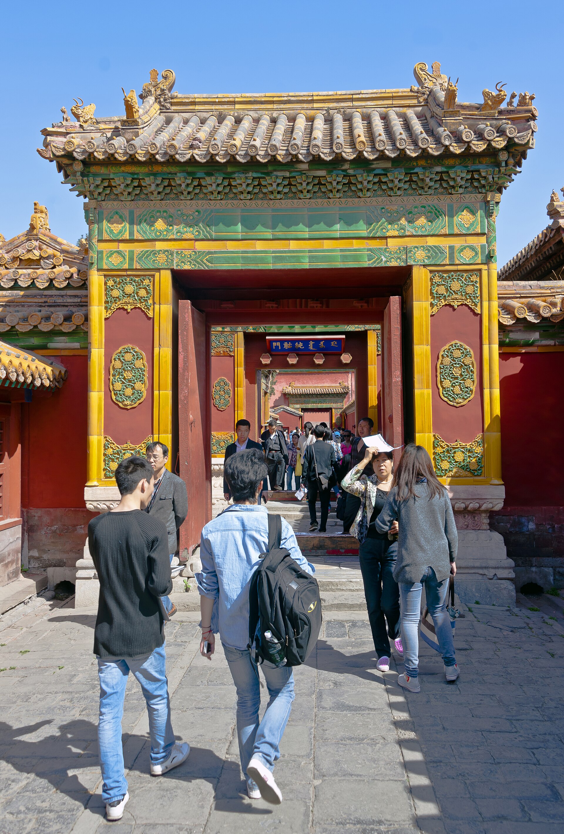 Ornate roofed gate through nested western-palace courtyards, with modern visitors beneath it.