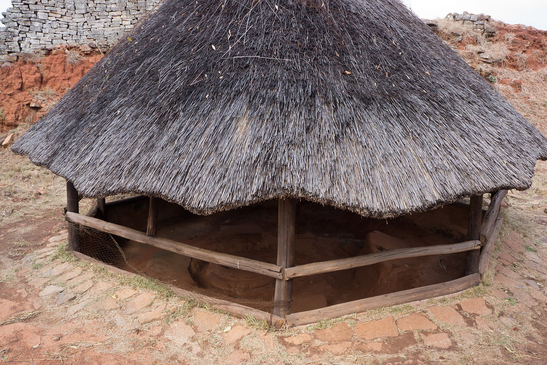 Modern roofed interpretive reconstruction of a house at Great Zimbabwe, with earthen interior below thick thatch.