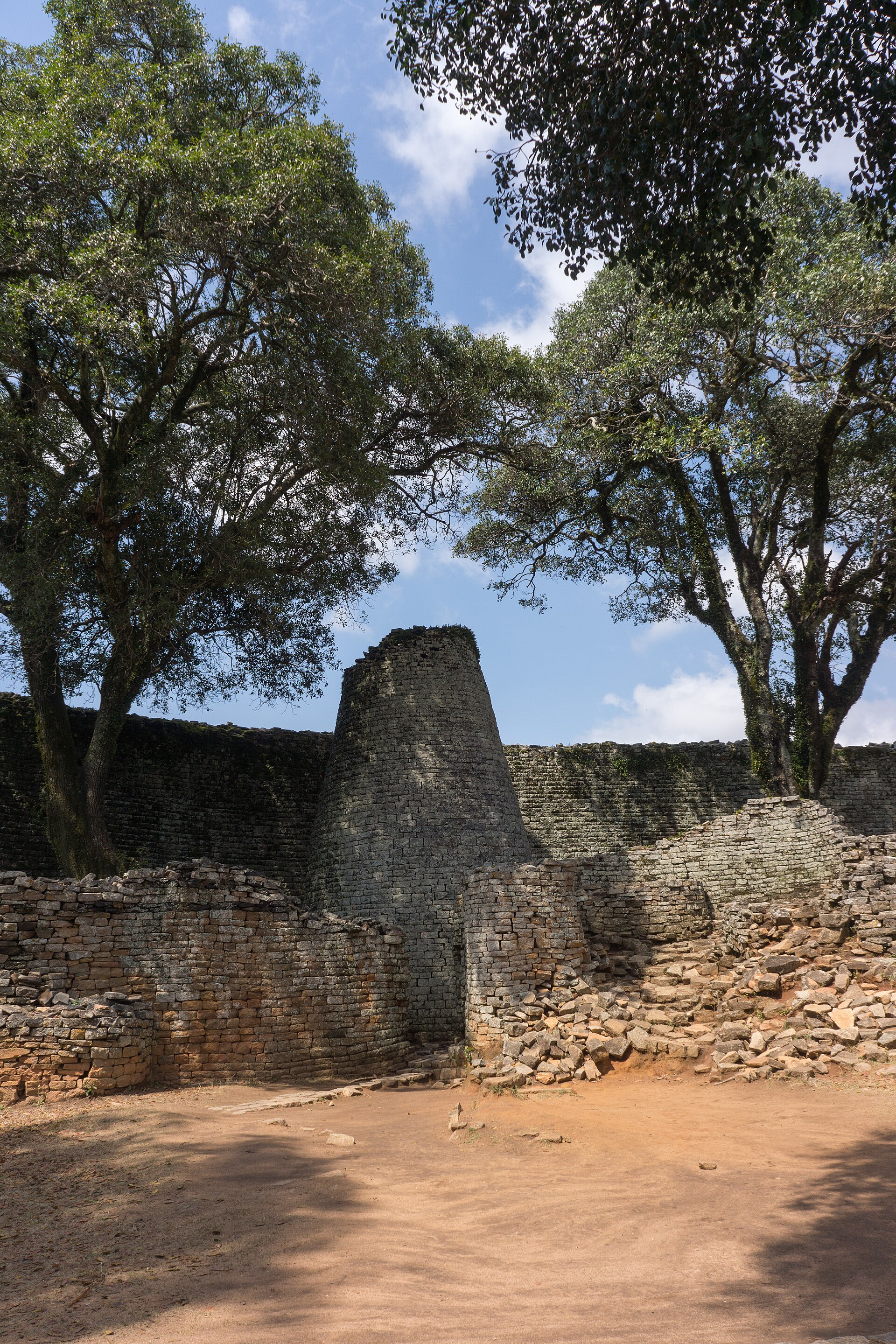 Solid conical stone tower within a Great Enclosure court, framed by trees and lower walls.