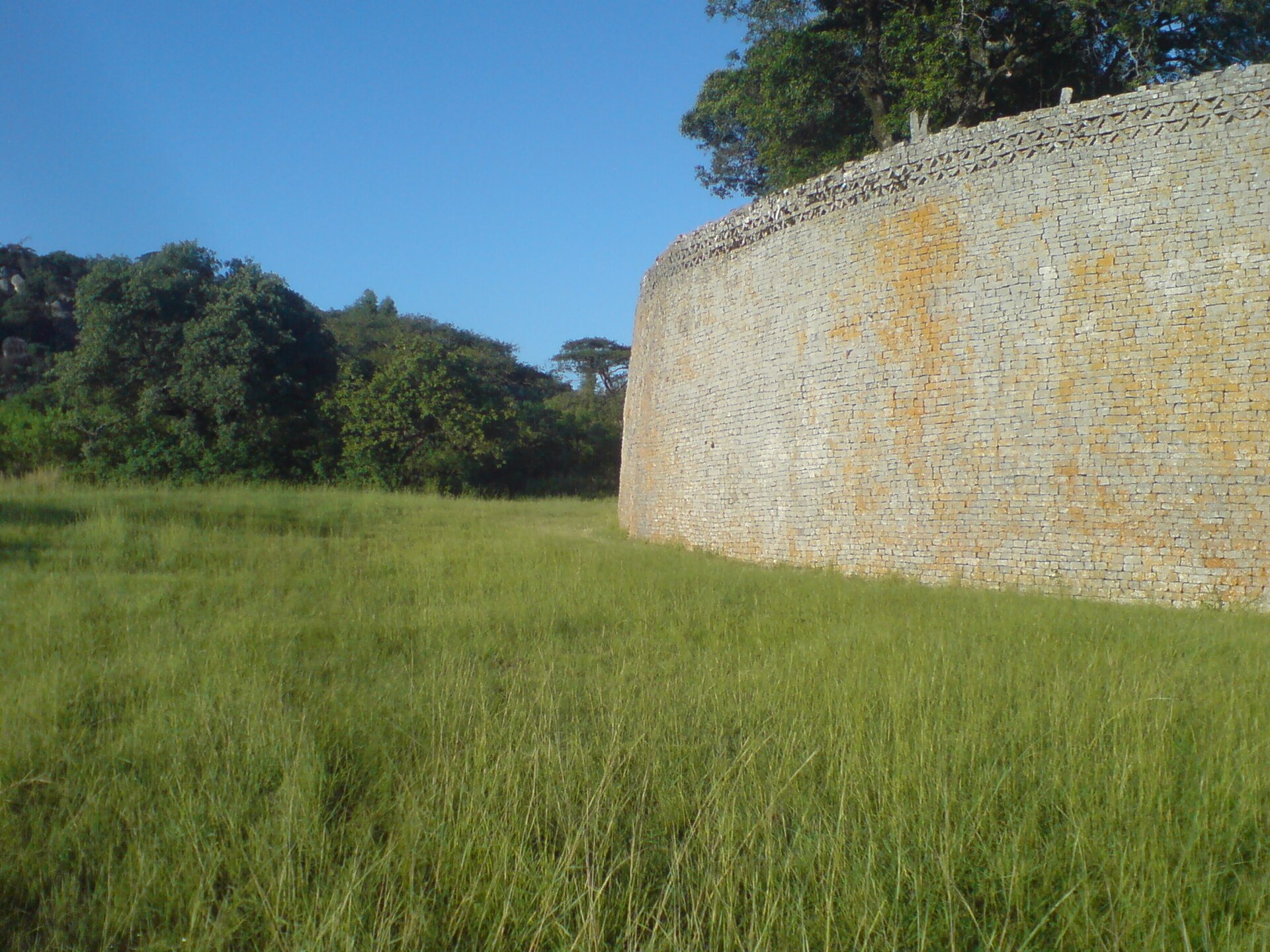 Tall coursed granite wall with geometric chevron pattern near its top.