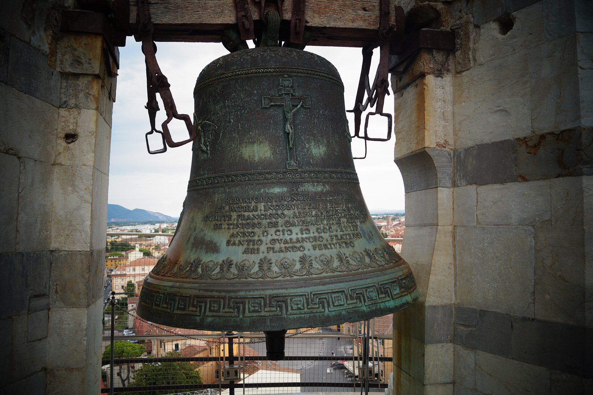 Large bronze bell hanging within an open stone arch of the Leaning Tower of Pisa belfry.