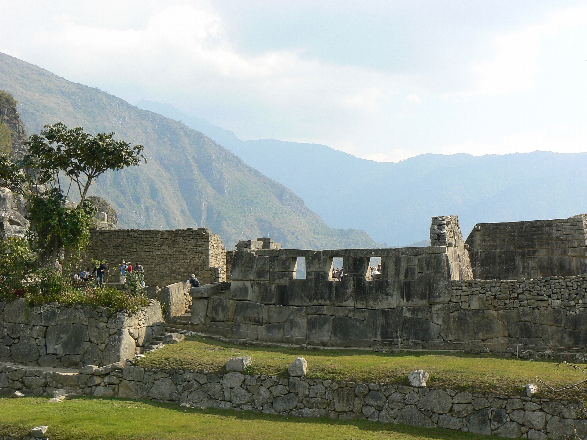 Inca stone enclosure with three large trapezoidal openings across its finely dressed upper wall and visitors beyond.