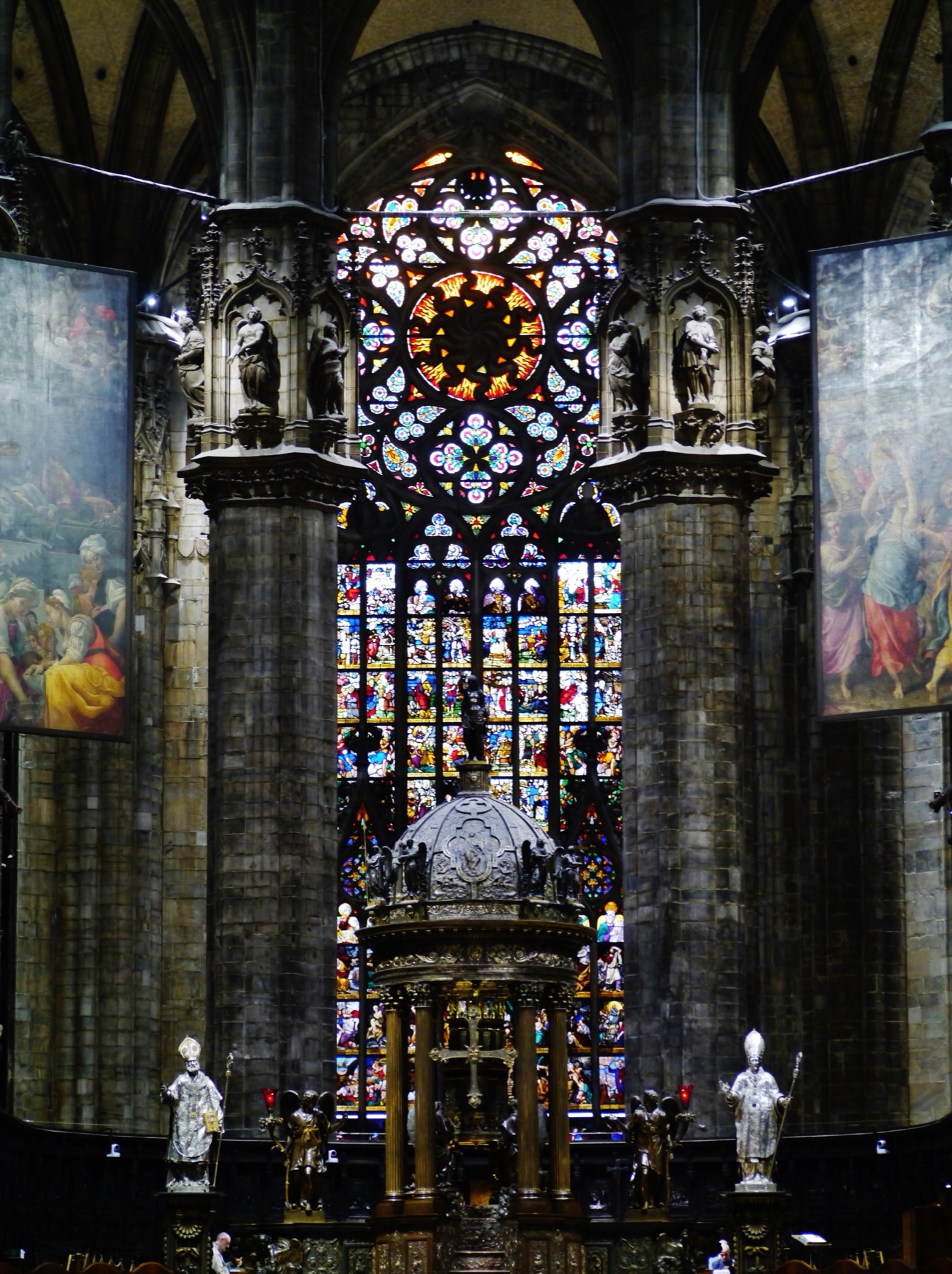 Milan Cathedral’s presbytery with Tibaldi’s domed tabernacle, episcopal figures, hanging paintings and the illuminated central apse window.