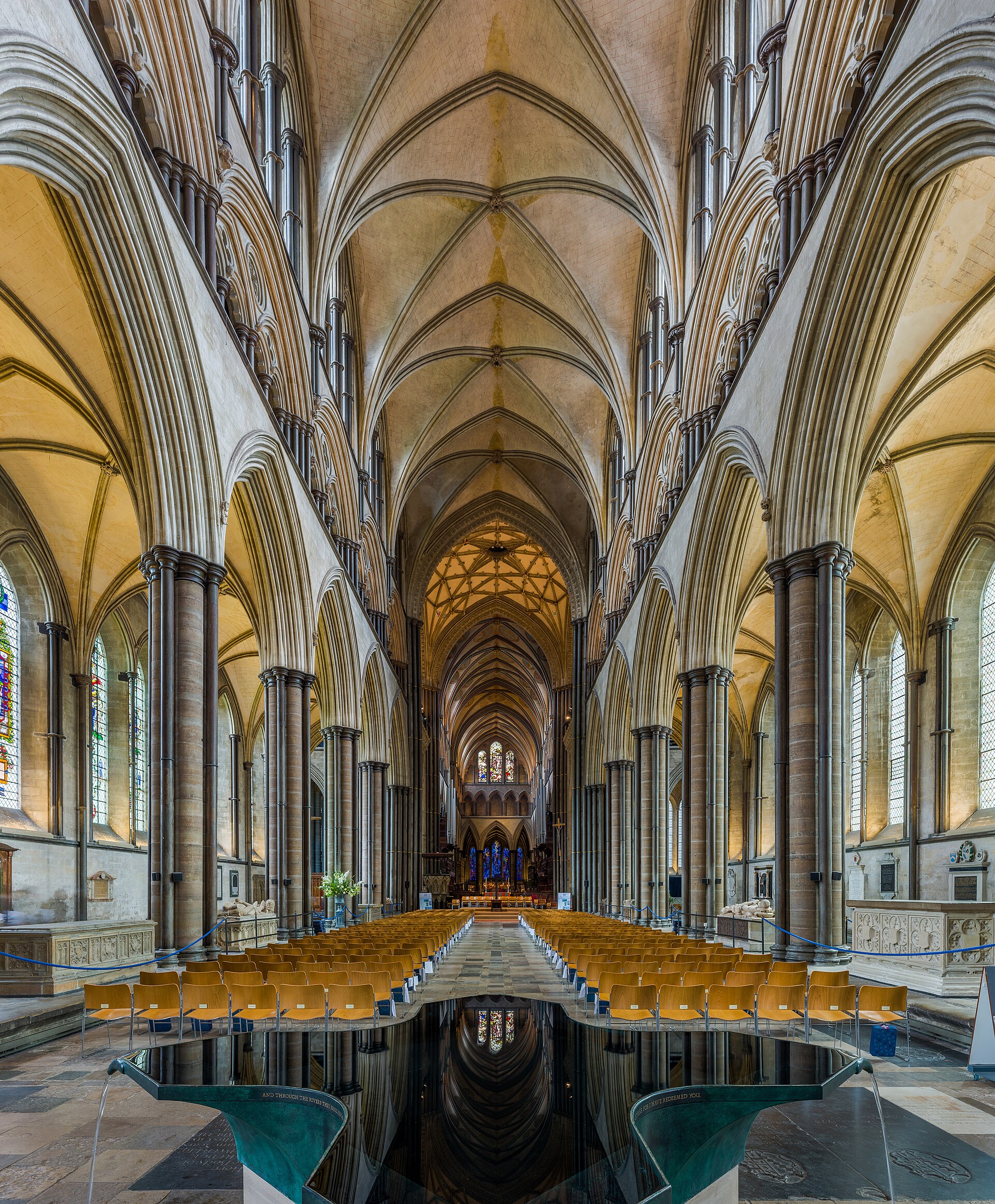 Salisbury Cathedral nave looking east past dark Purbeck shafts, pointed arcades and gallery to the choir, with William Pye's reflecting font in the foreground.