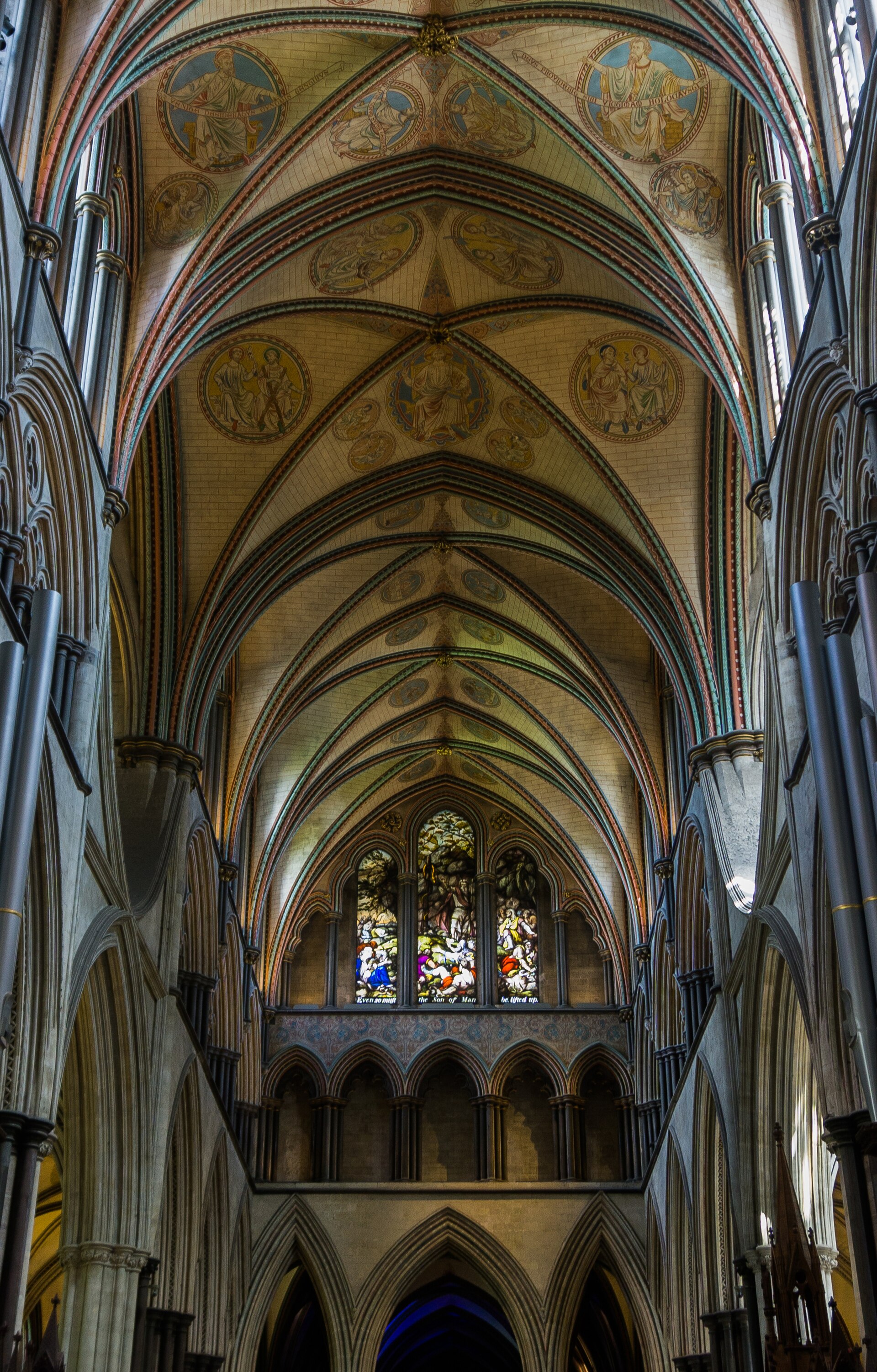 Painted rib vaults with roundels of prophets and sacred figures above dark shafts in Salisbury Cathedral's eastern interior.