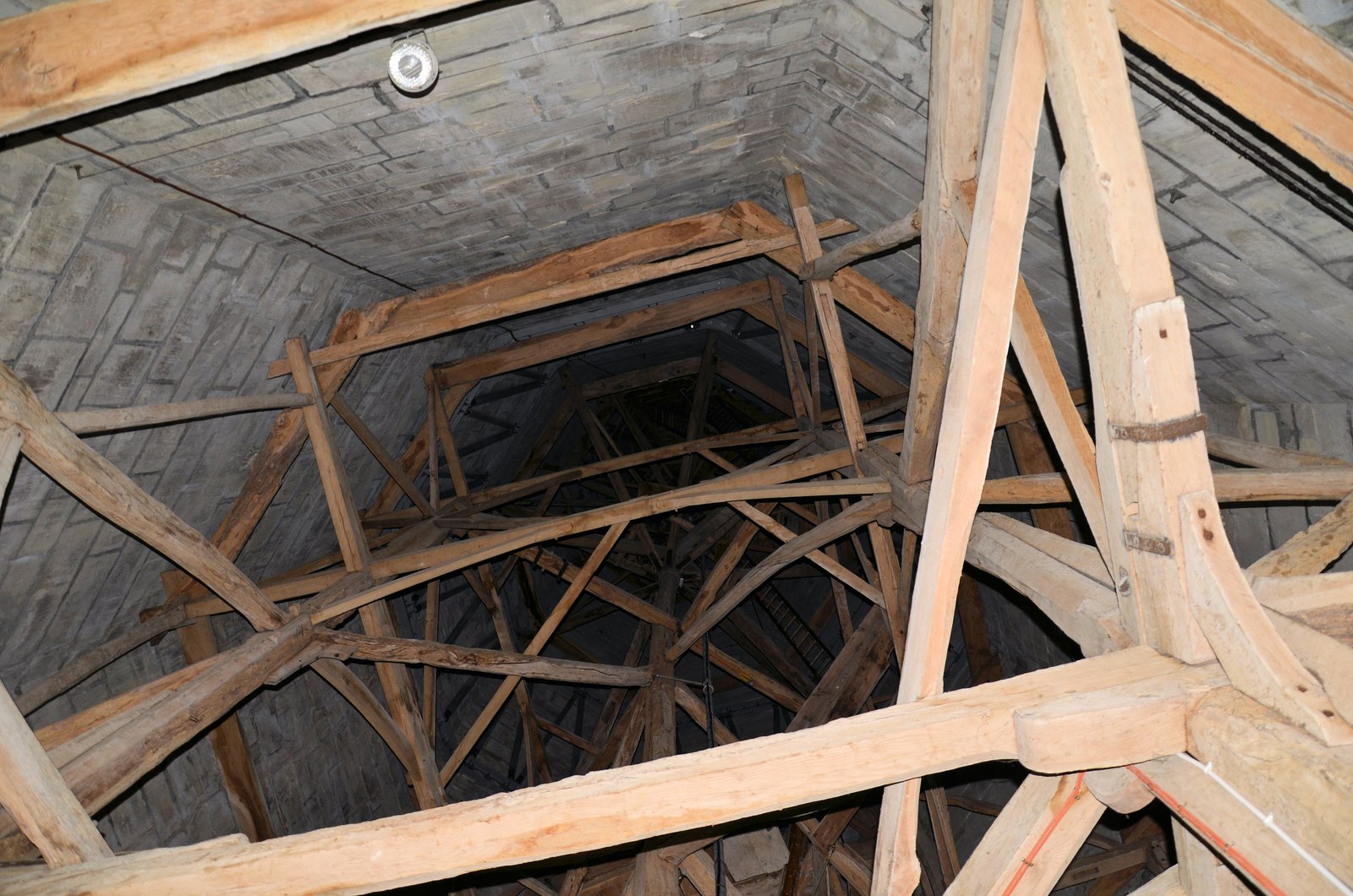Dense oak posts and diagonal braces rising within the narrowing grey masonry shell of Salisbury Cathedral's spire.