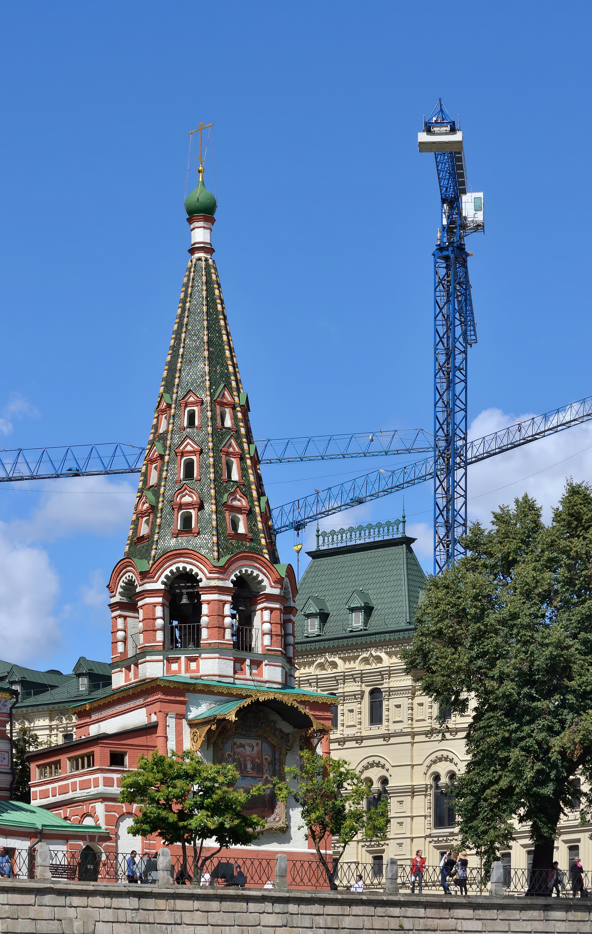 Seventeenth-century bell tower at St Basil’s Cathedral, with bells in lower openings and modern cranes beyond.