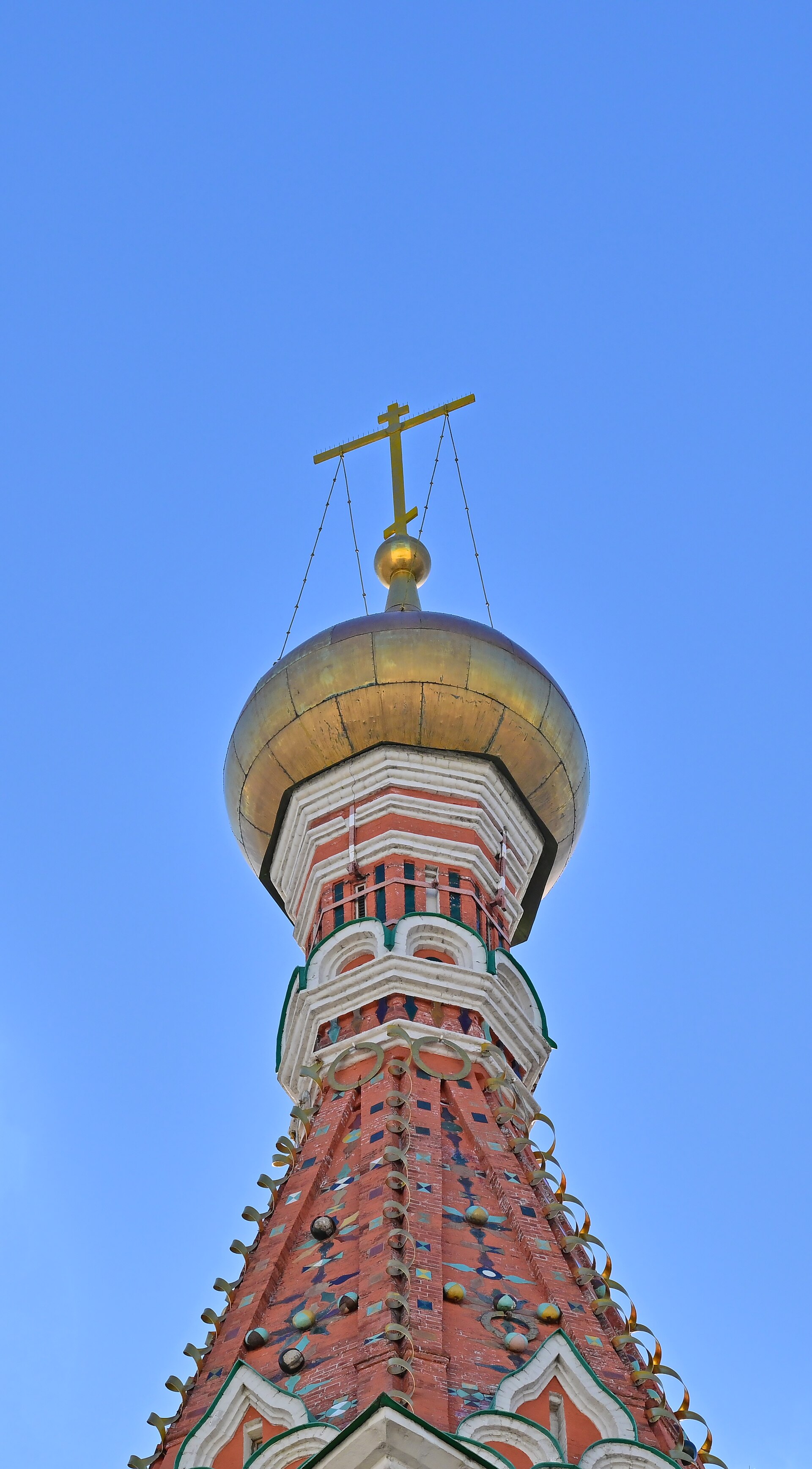 Close view upward along the central tent roof with coloured tile-like surfaces, metal spiral ornament and golden head.