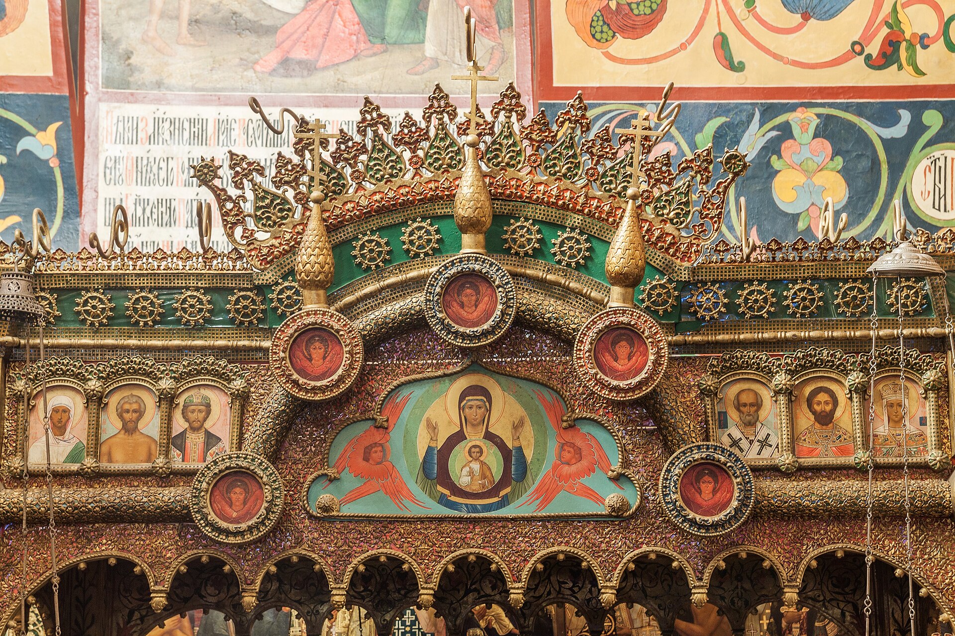 Close detail of a richly ornamented iconostasis with sacred figures and wall painting inside a cathedral church.