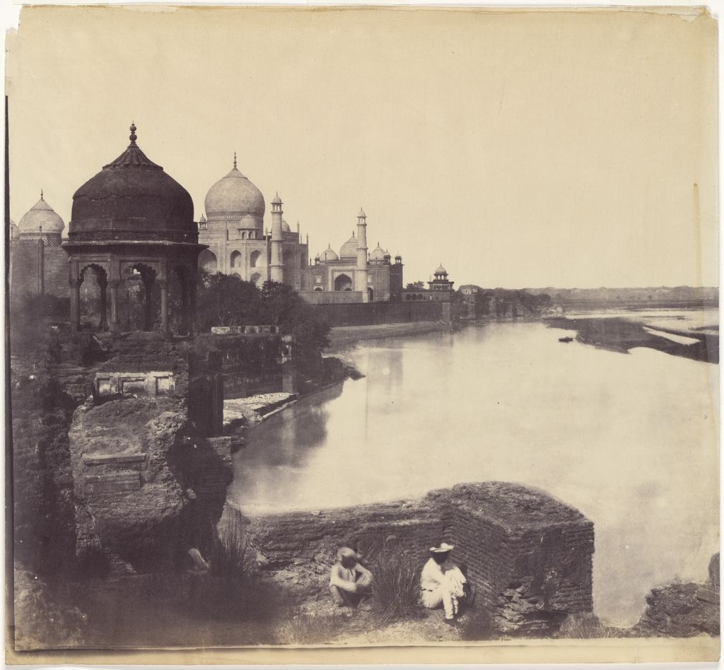 A faded nineteenth-century photograph looks along a broad river toward the Taj Mahal, with a dark domed pavilion, old bank walls and two seated figures in front.