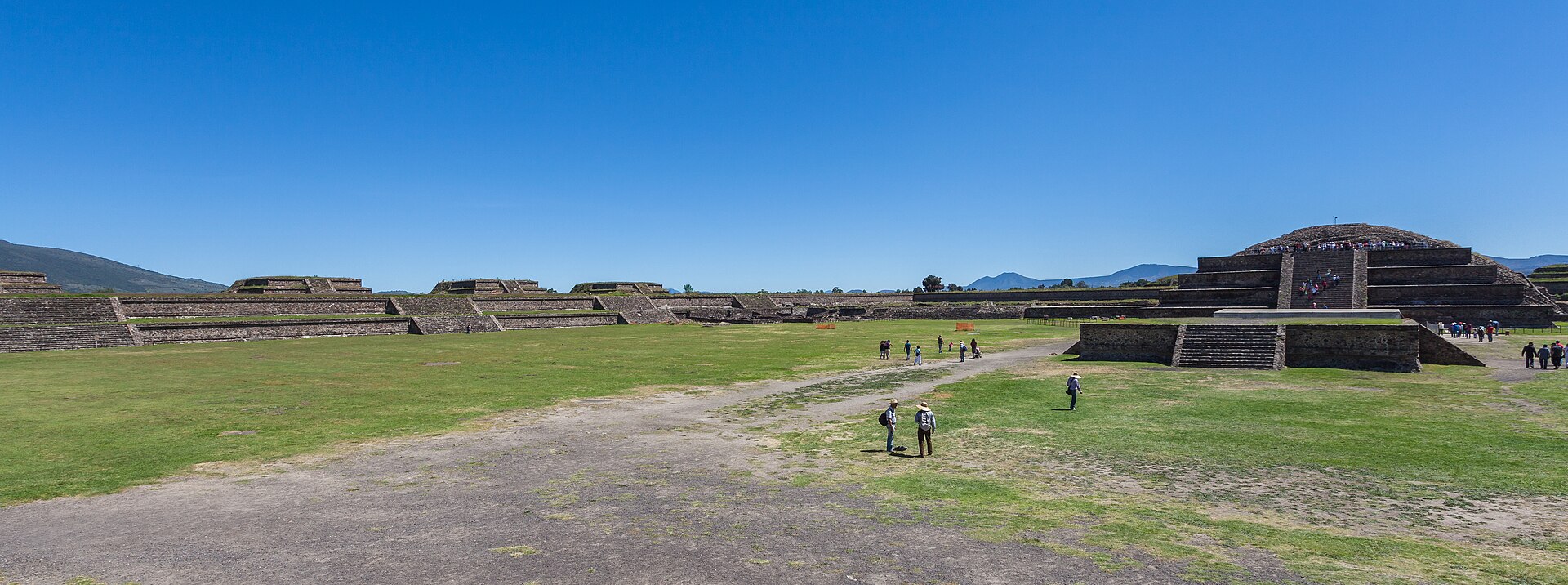 Wide panoramic view across the Ciudadela grassy court towards a stepped monument and surrounding low platforms.