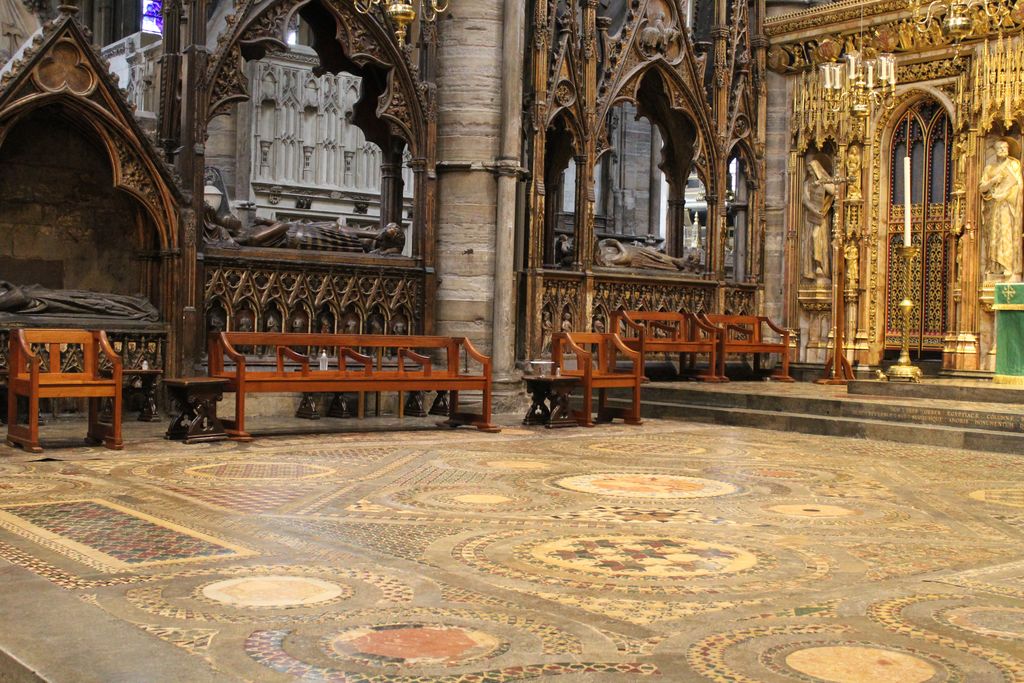 A broad medieval floor of coloured stone and glass forms large circles, interlacing bands and rectangular geometric fields before an ornate sanctuary.