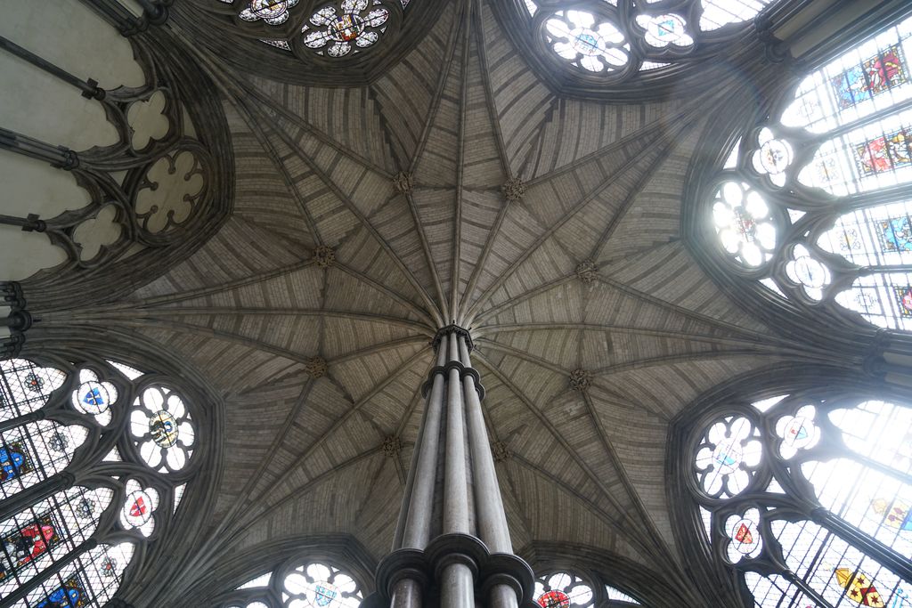 A clustered stone column rises into many ribs that fan across an octagonal vault surrounded by large traceried windows.