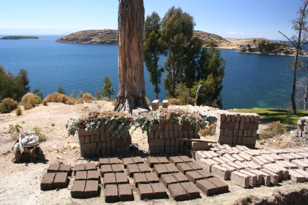 Rows and stacks of rectangular adobe units on drying ground beside Lake Titicaca.