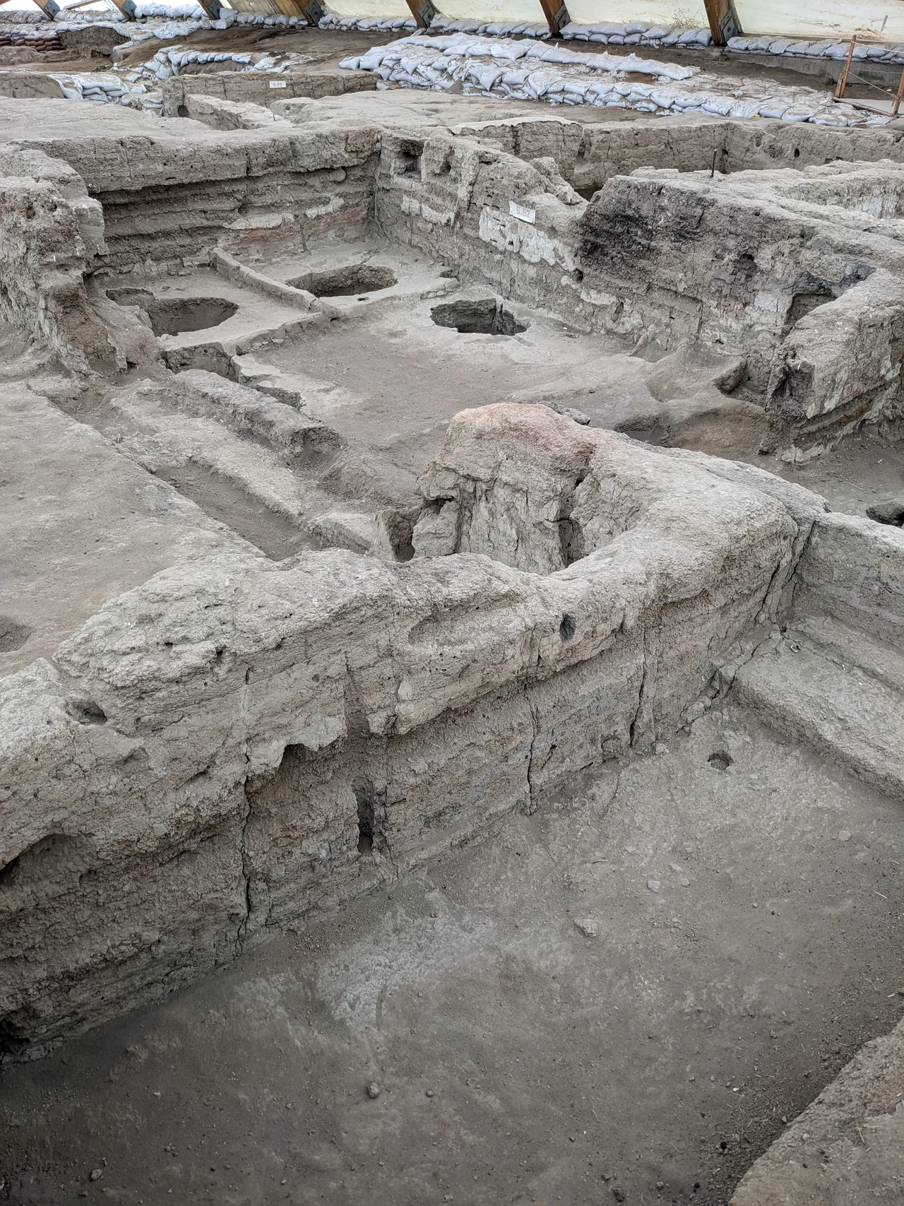 Sheltered excavations at Çatalhöyük with earth wall edges, floor traces and modern sandbags.