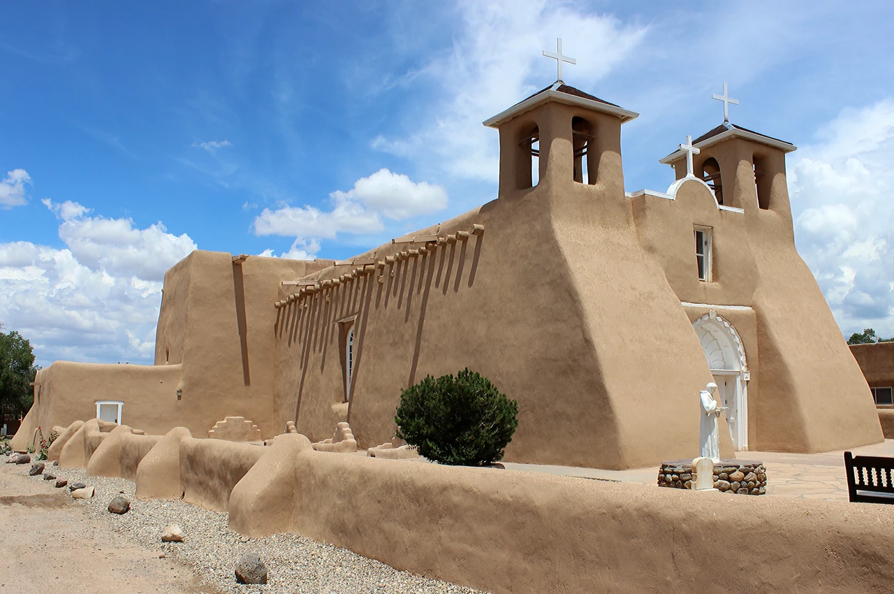 Front and side of Ranchos de Taos church with paired towers, buttresses, timber ends and white trim.