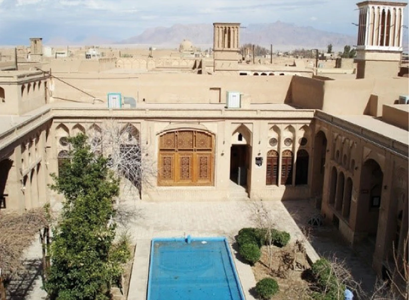 Lariha house courtyard with a blue pool, trees, arcaded rooms and windcatchers.
