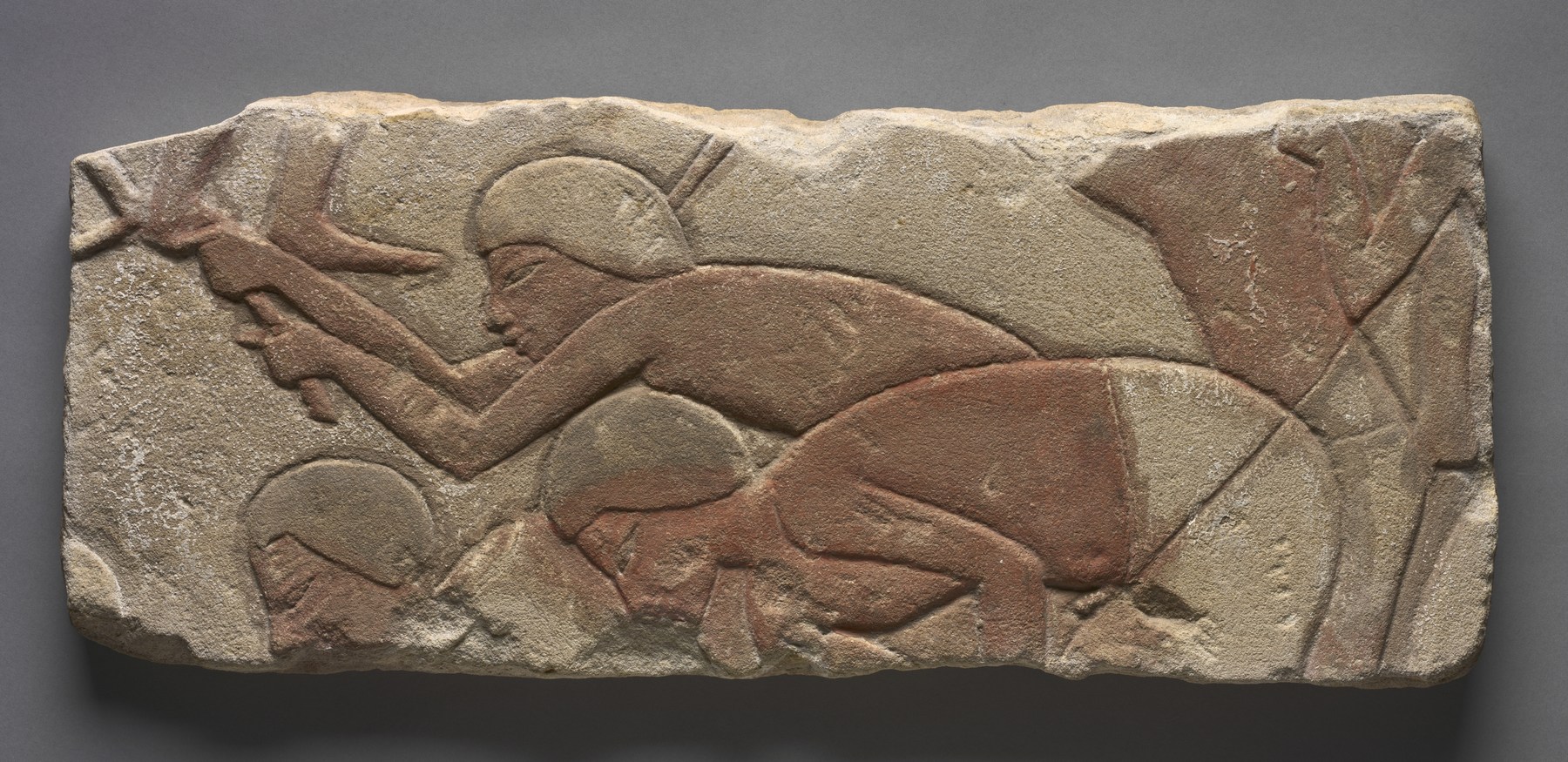 Painted sandstone talatat fragment showing ancient Egyptian workers raising hoes to prepare earth.