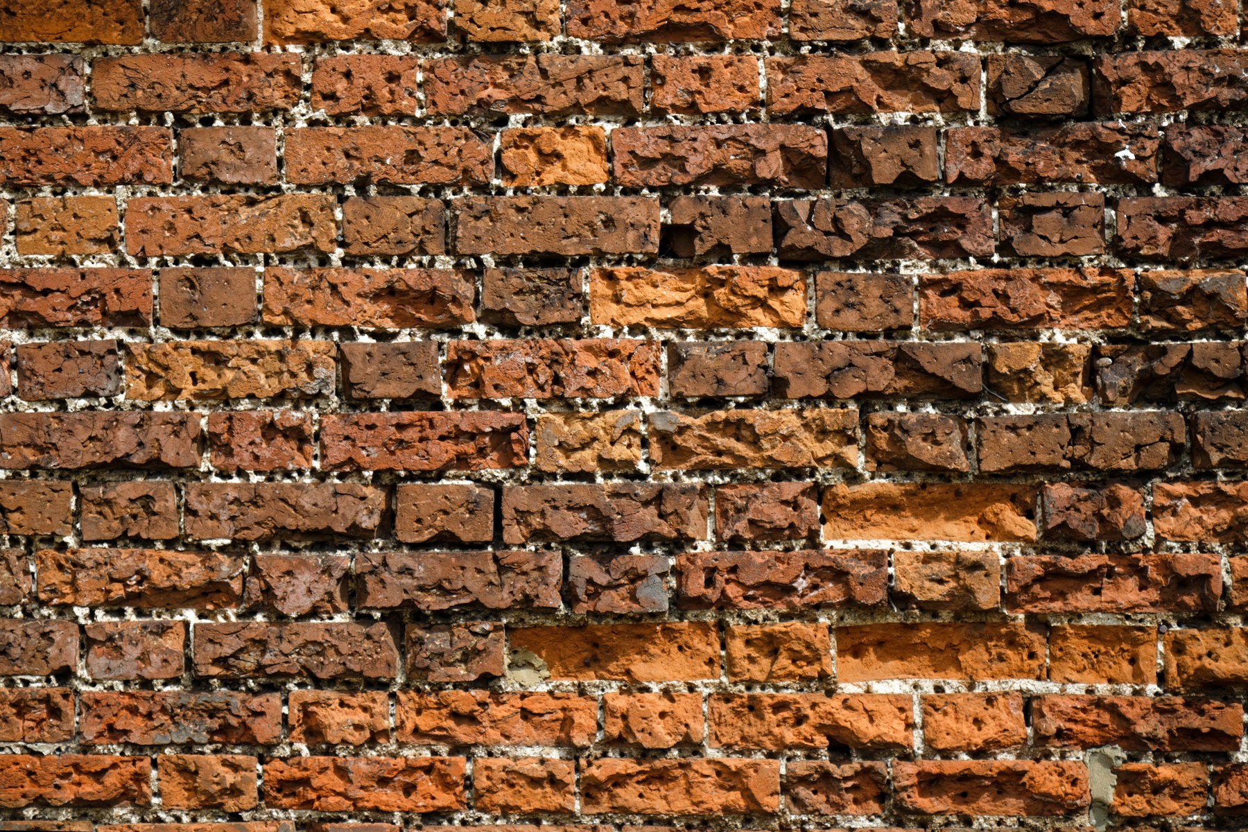 Close view of orange, brown and dark brick faces, alternating long and short rectangles, with uneven grey mortar joints.