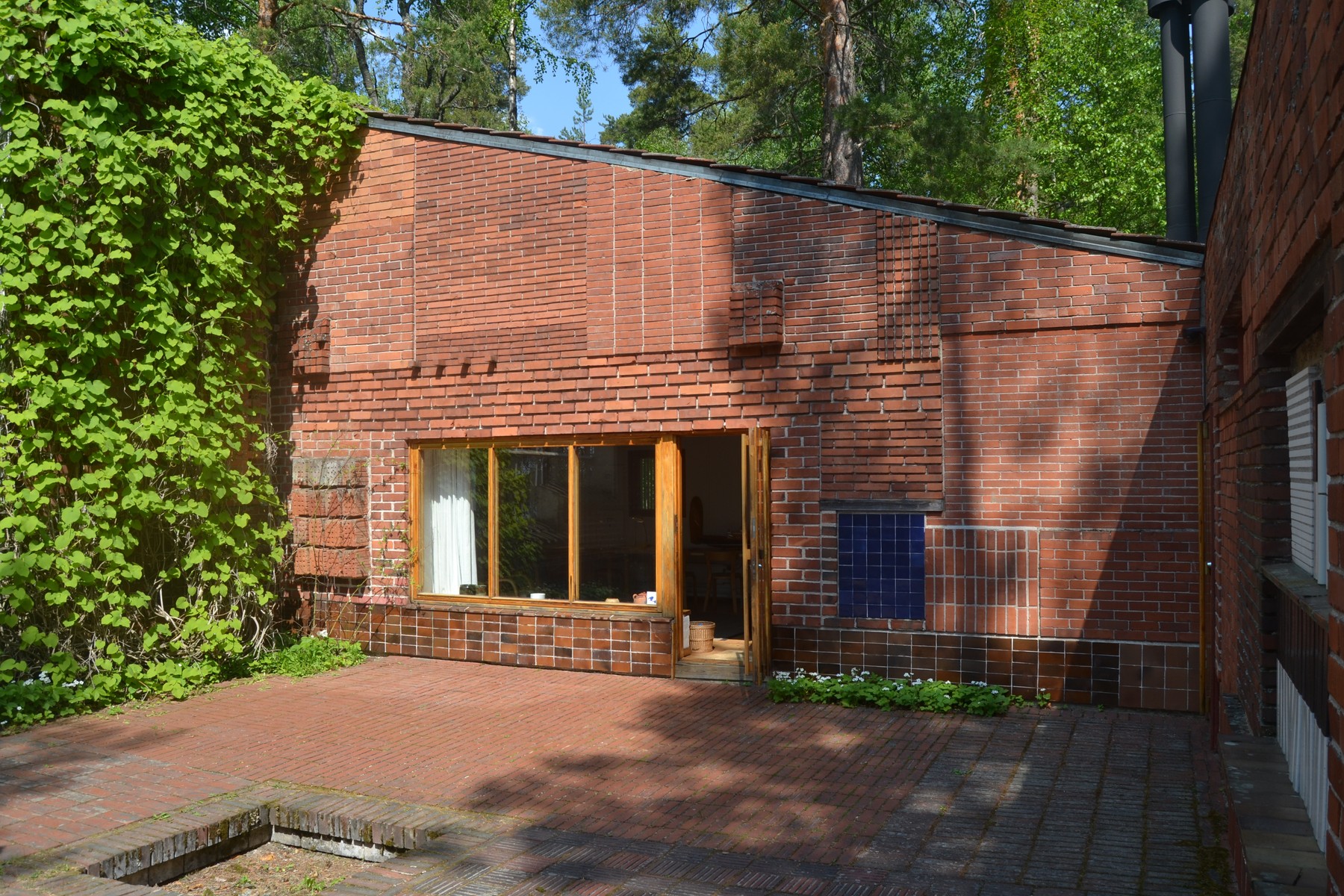 Courtyard walls and paving with varied brick patterns, a blue square-tile panel, windows, a wooden door and plants.