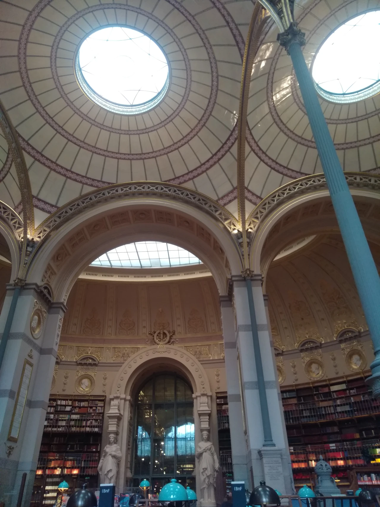 Blue-green slender columns rise beside bookshelves to decorated domes with round openings in Richelieu’s Salle Labrouste.