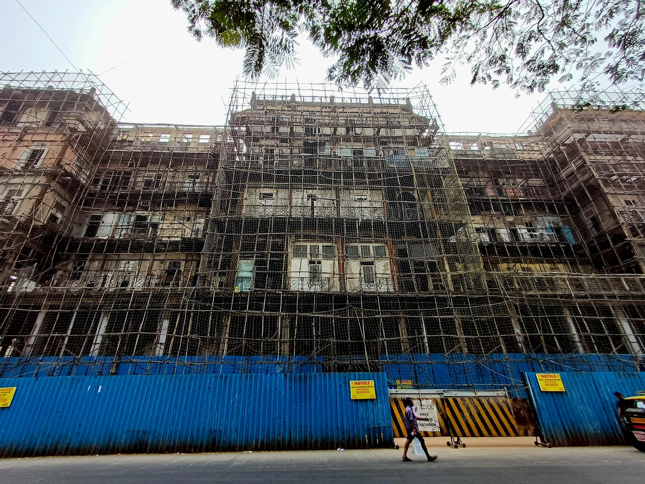 Scaffolding covers Watson’s Hotel above a blue street barrier, with stacked balconies visible through the temporary structure.