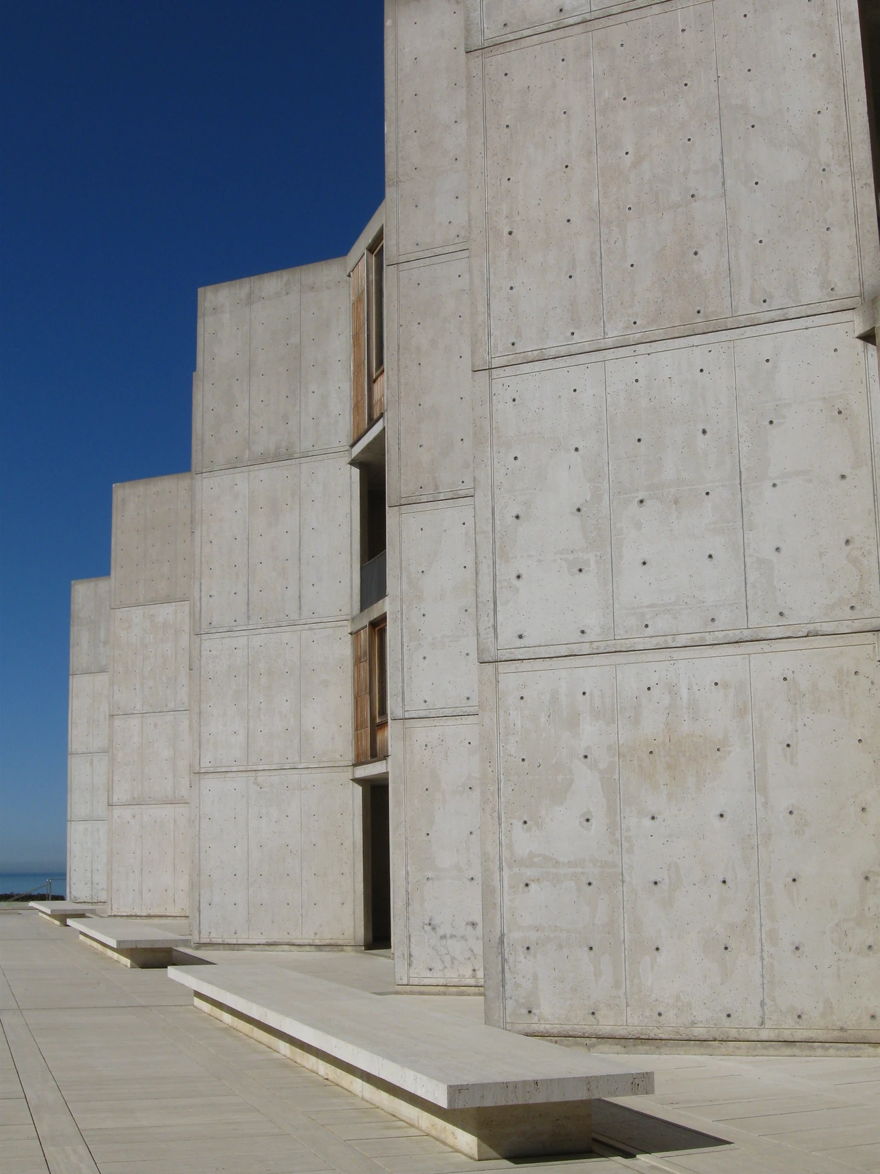 Concrete wall faces show a grid of panel divisions and repeated circular marks, with narrow strips of timber and steps below.