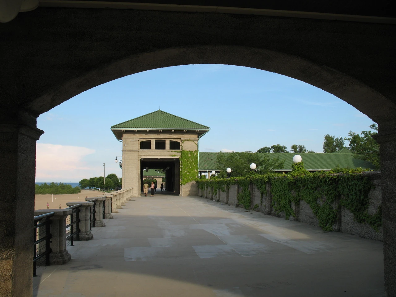 An arch frames a bathing-pavilion passage leading towards a roofed tower, with weathered parapets and planting along the side.