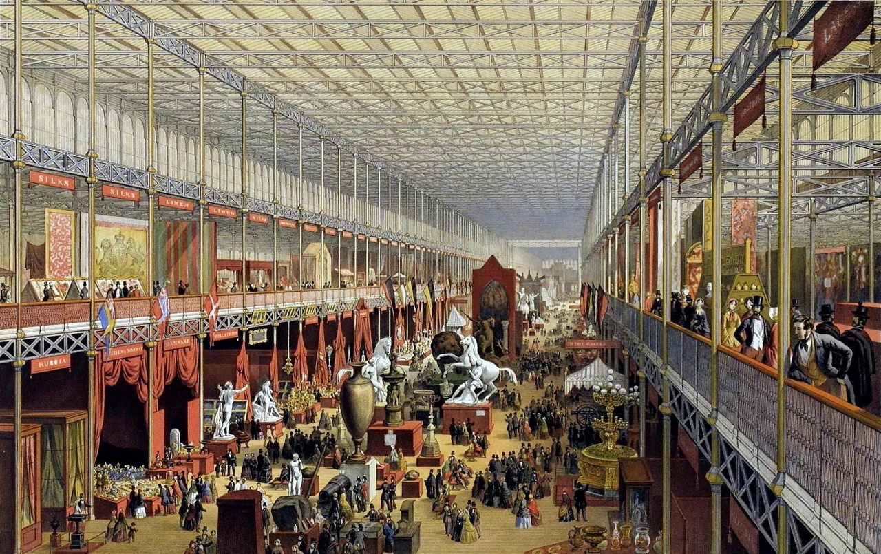 A coloured 1851 view of the Crystal Palace interior, with a high glazed roof, galleries, displays and crowds.