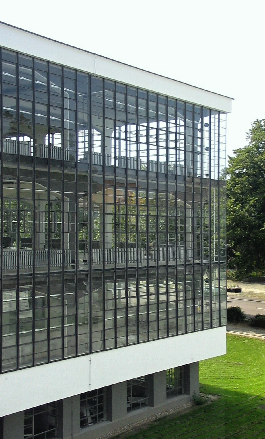 The glazed corner of the Dessau Bauhaus workshop wing shows repeated steel-profile glazing, reflections and parts of the interior structure.