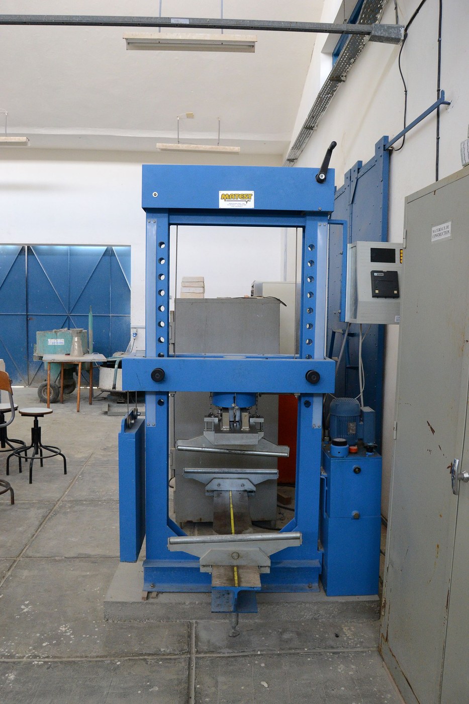 Blue laboratory compression-testing machine used to measure the resistance of a concrete specimen.