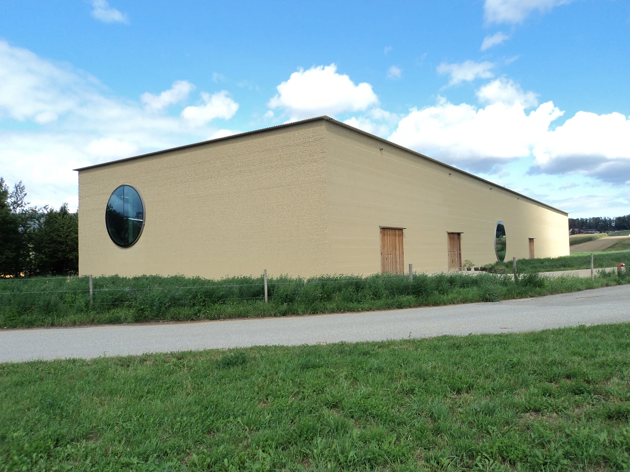 Ricola herb centre corner with horizontal earth bands, two round windows and timber doors.