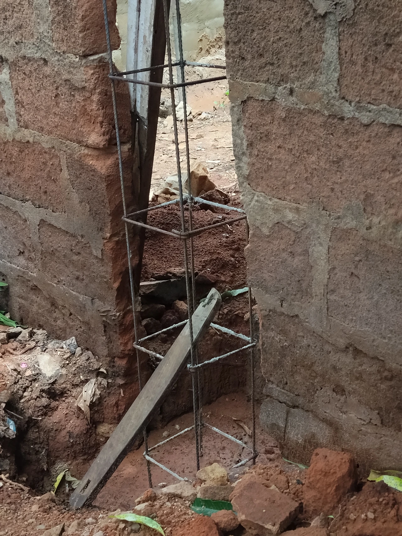 Vertical bars joined by rectangular transverse loops stand between masonry faces before a pillar is cast.
