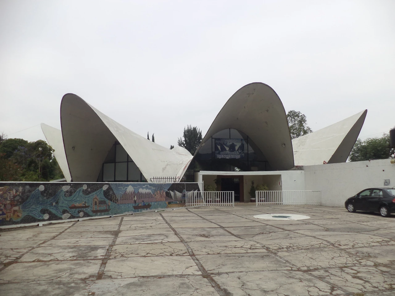 Curving concrete roof lobes rise over the street-facing entry and forecourt of Los Manantiales.