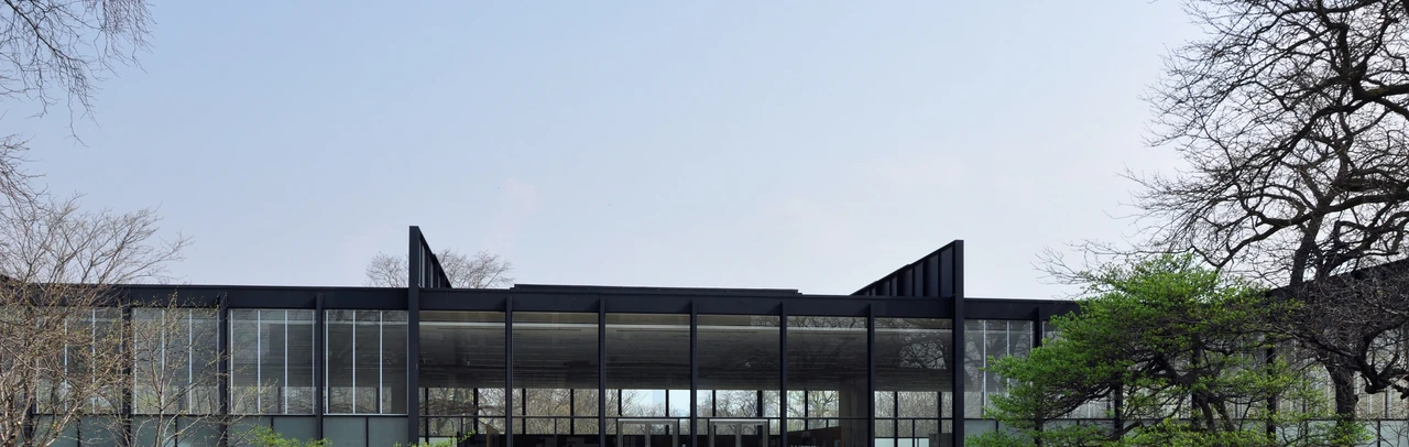 Deep dark girders project above Crown Hall’s glazed teaching hall, with trees framing the roofline.