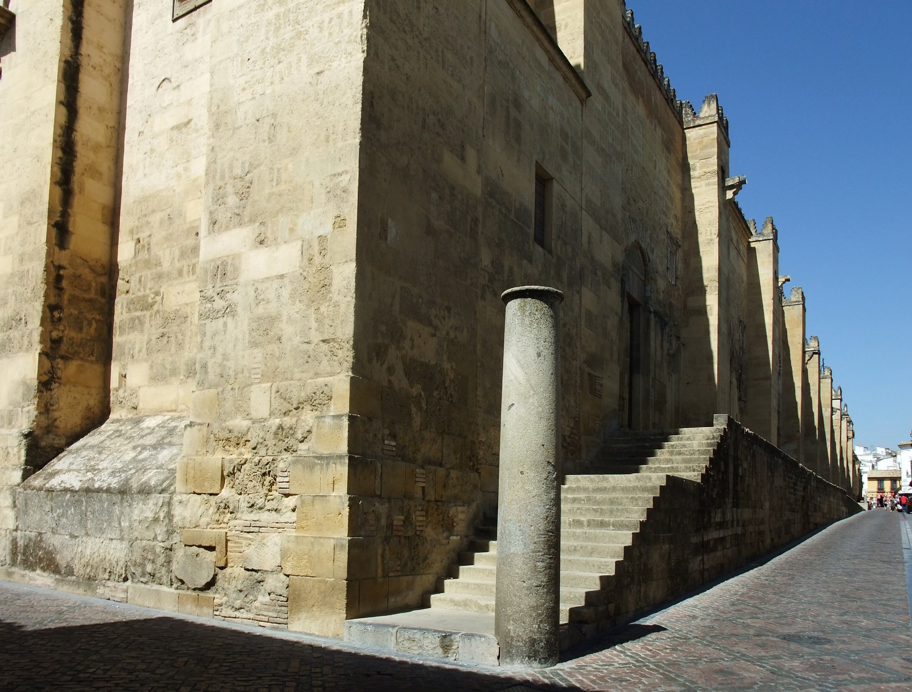 Stone wall and buttresses of the Mosque of Córdoba with steps and a column beside an opening.