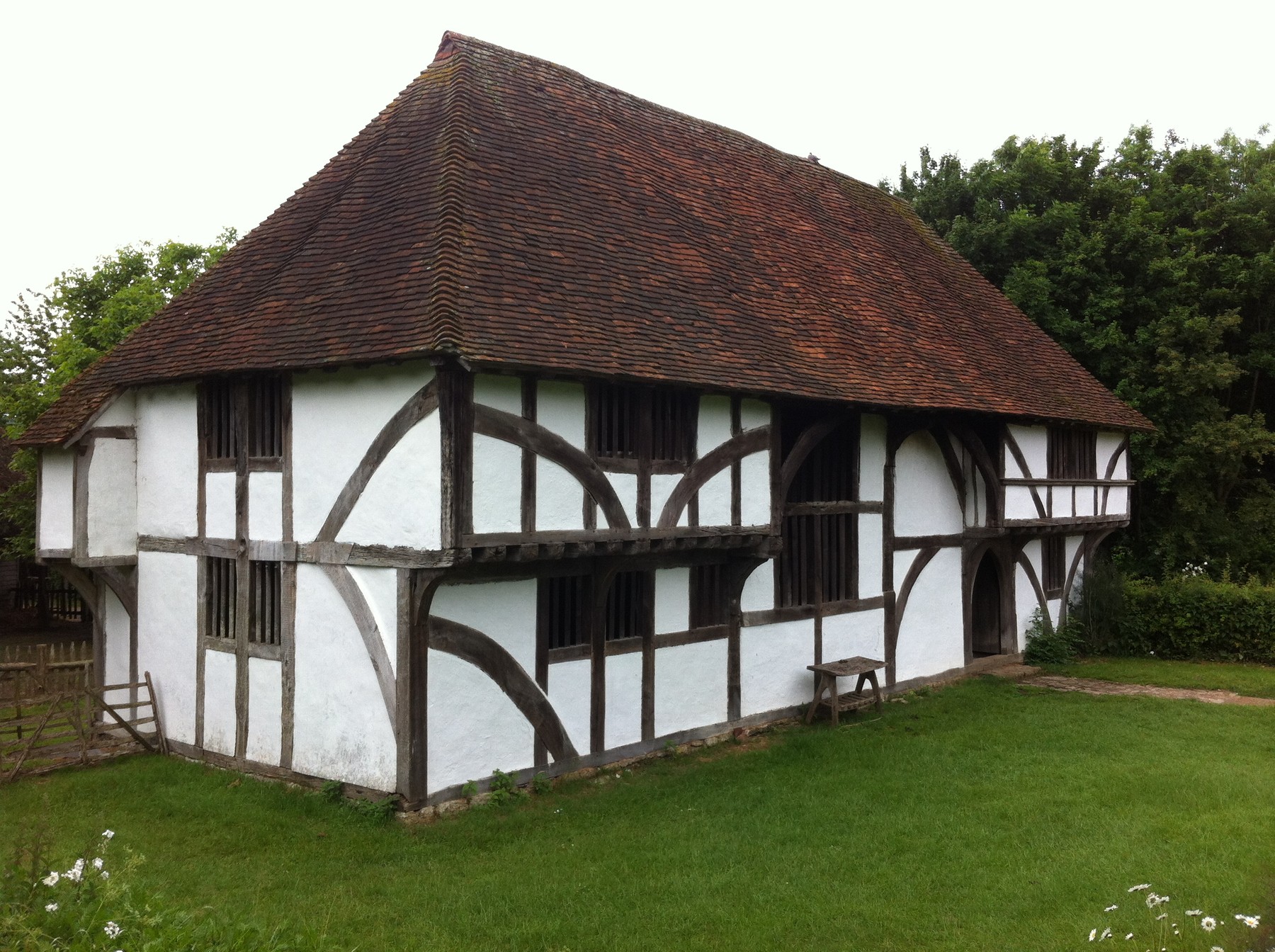Bayleaf farmhouse with dark timber members, white infill, jettied ends and a recessed central hall beneath a tiled roof.