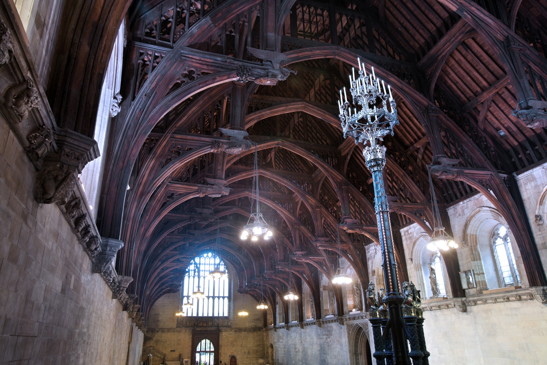 Arched timber roof and carved hammerbeam ends above Westminster Hall's stone walls.