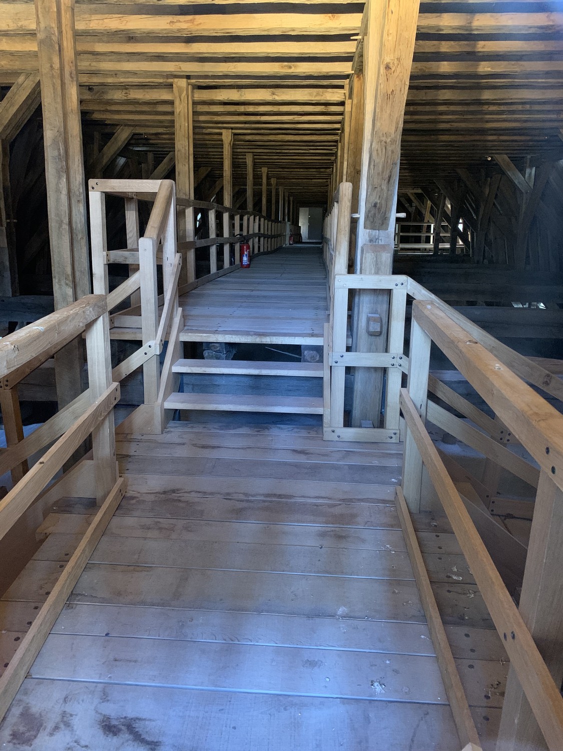 Pale new timber members, a modern walkway and handrails inside Notre-Dame's reconstructed roof space.