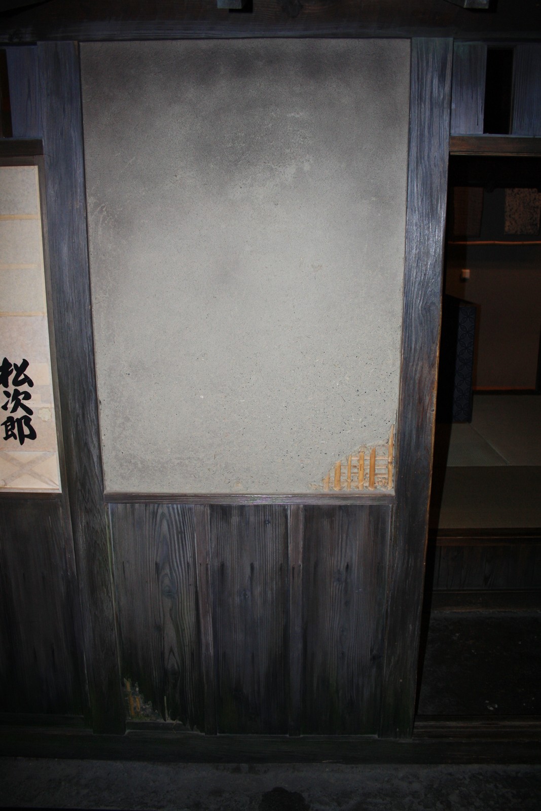 A finished earth-coloured panel in a dark timber frame at Fukagawa Edo Museum, with a small lower-right cutaway exposing supports.