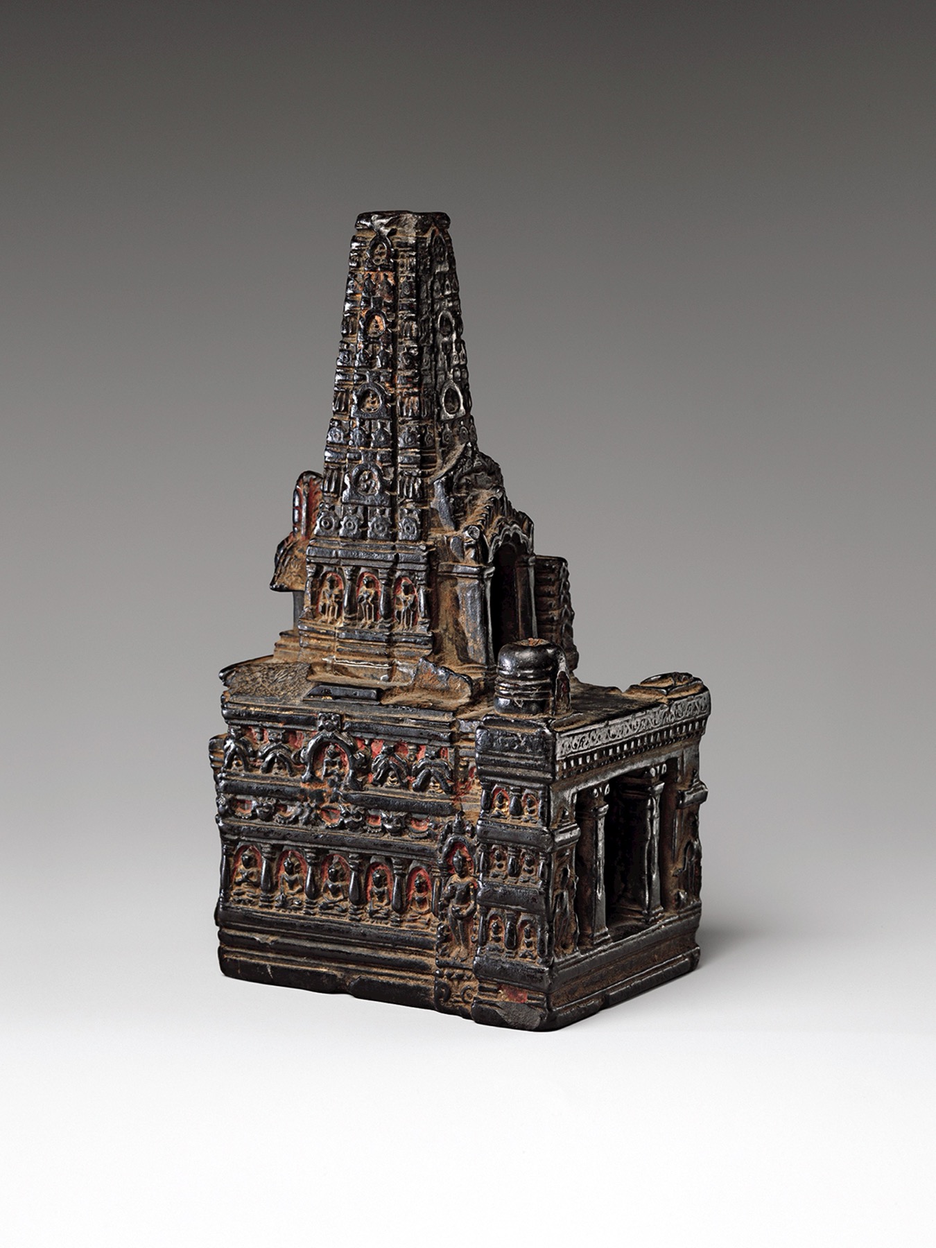 Dark carved stone miniature of a towered Indian temple on a low rectangular base.