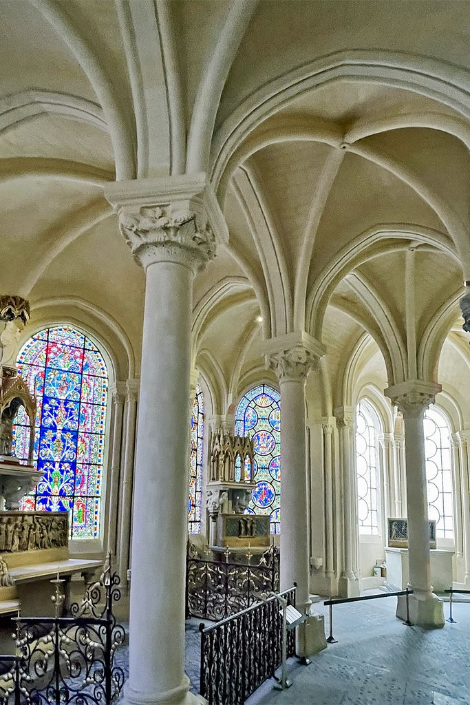 Slender columns and branching vault ribs stand before stained-glass chapels, with iron railings and a belt barrier below.