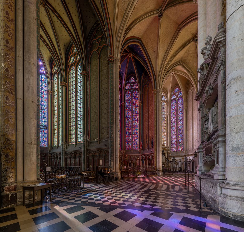 A broad tiled passage curves past columns and glazed chapels under ribbed vaults, beside a carved wall monument.