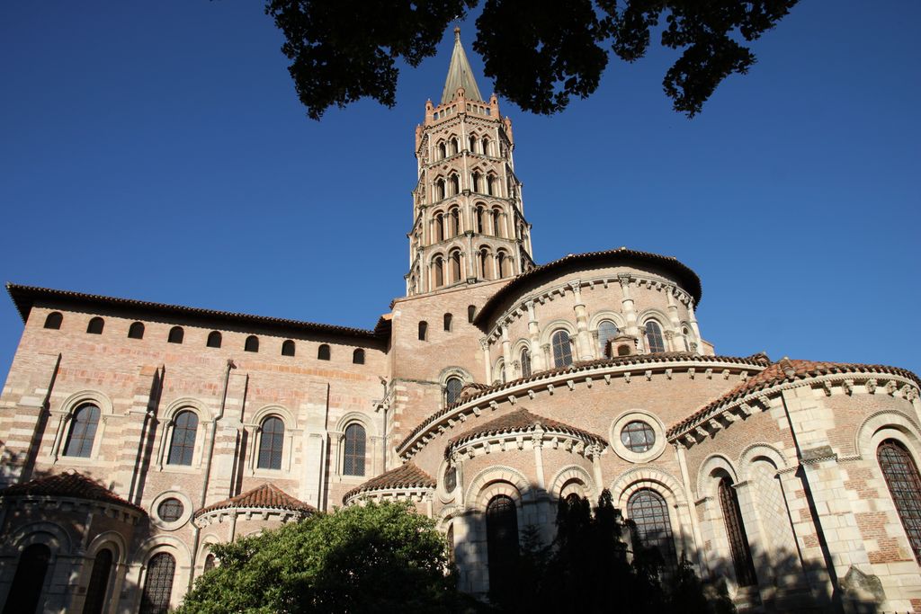 A tall curved apse rises above a lower curving roof and smaller rounded chapels, with a transept and tiered tower behind.