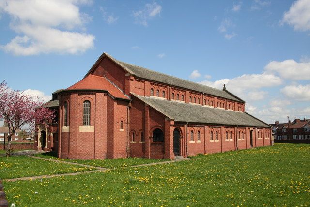 A rounded red-brick projection with three tall arched windows and a tiled roof stands at the near end of a long brick church.