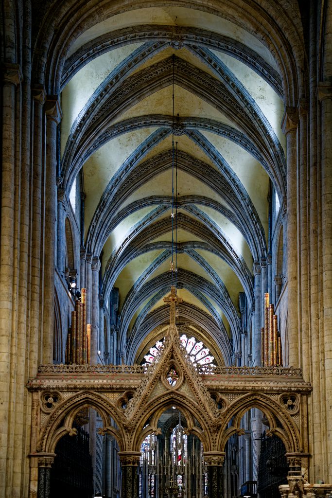 A carved screen with three pointed openings and a central cross stands beneath a long sequence of tall ribbed vaults.