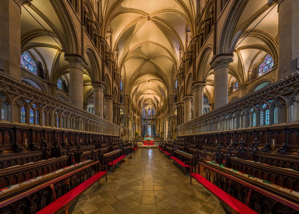 Two facing rows of carved stalls and red cushions flank a paved aisle beneath high arcades and rib vaults, with a raised altar-side area beyond.